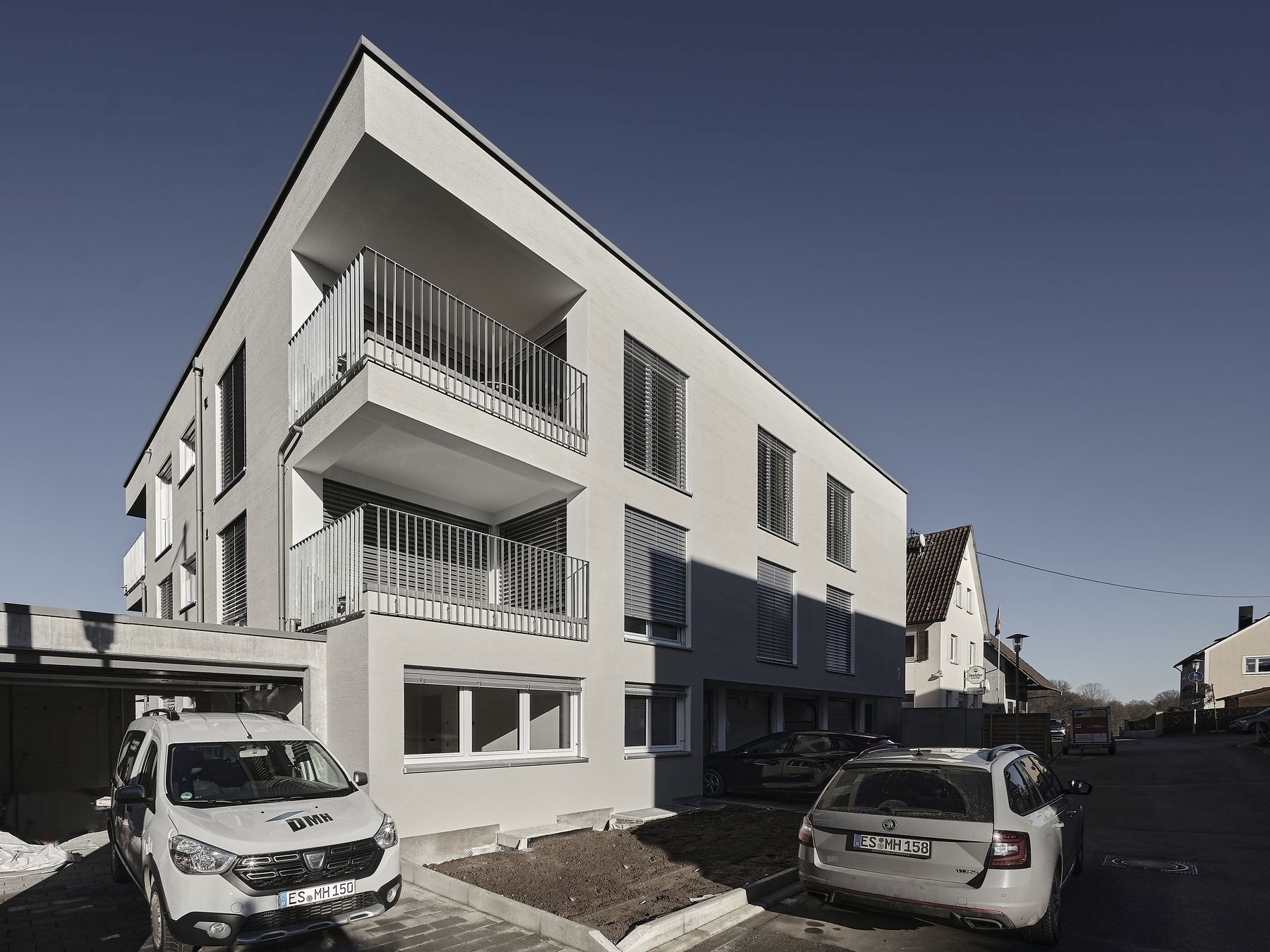 Modernes Mehrfamilienhaus mit Flachdach, eigeschnittenen Balkonen und Jalousien
